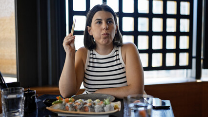 Young beautiful hispanic woman eating sushi at the restaurant