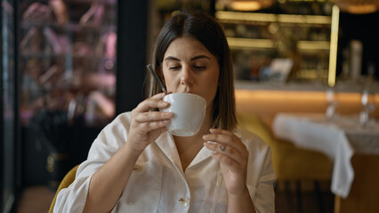 Young beautiful hispanic woman drinking coffee sitting on the table at the restaurant