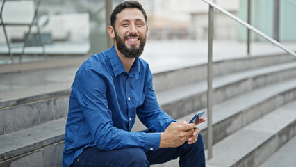 Young hispanic man business worker using smartphone sitting on stairs at street