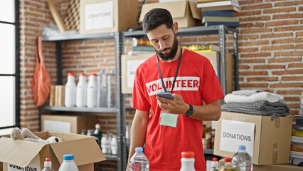 Young hispanic man volunteer using smartphone at charity center