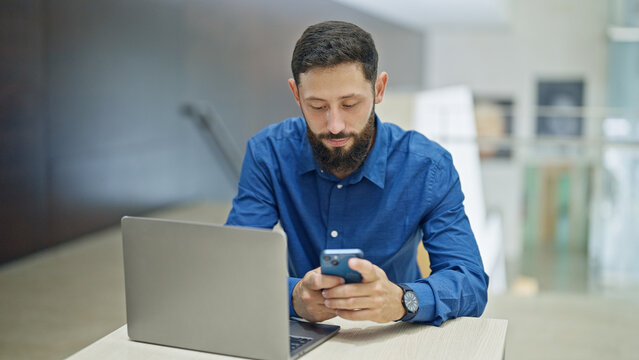 Young hispanic man business worker using laptop and smartphone working at the office