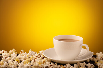 Cup of tea with popcorn on yellow background with text space