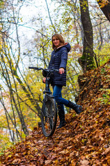 A young woman with a bicycle on a forest trail in the autumn forest