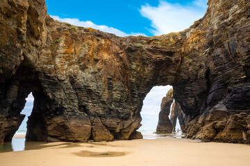 Natural rock arches Cathedrals beach, Playa de las Catedrales at Ribadeo, Galicia, Spain. Famous beach in Northern Spain Atlantic. Natural rock arch on Cathedrals beach in low tide - obrazy, fototapety, plakaty