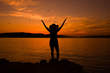 Sylwetka kobiety z otwartymi ramionami przed zachodem słońca.