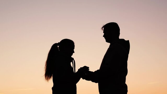 Silhouette man gives gift to his beloved woman outdoors against sky. Young guy gives box with surprise to his girlfriend, happy couple hugs, gentle kiss in nature. Valentines Day. Romantic love, park