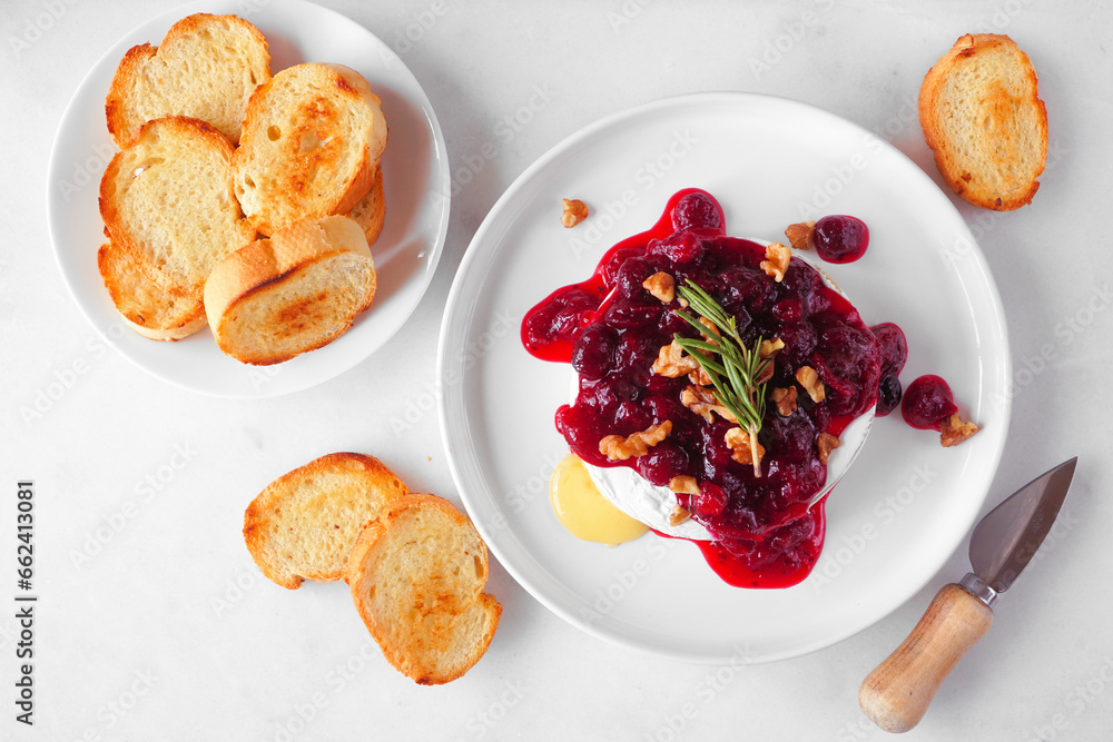 Poster baked brie appetizer garnished with cranberry sauce and walnuts. overhead view table scene with toas