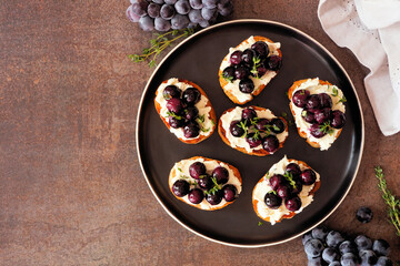 Crostini appetizers with roasted grapes and whipped feta cheese. Above view table scene against a dark background. Party food concept.