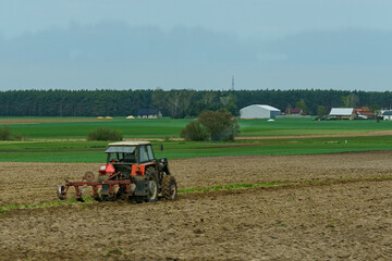 A tractor with plows stands near a plowed field.