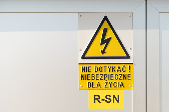 On a metal cabinet with electrical equipment there is a yellow warning sign with a lightning bolt and an inscription in Polish - Danger to life.