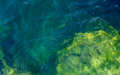 Fototapeta na wymiar Steine und Felsen unter Wasser mit Algen oder Moos bedeckt. Natürlich reflektiertes Sonnenlicht.
