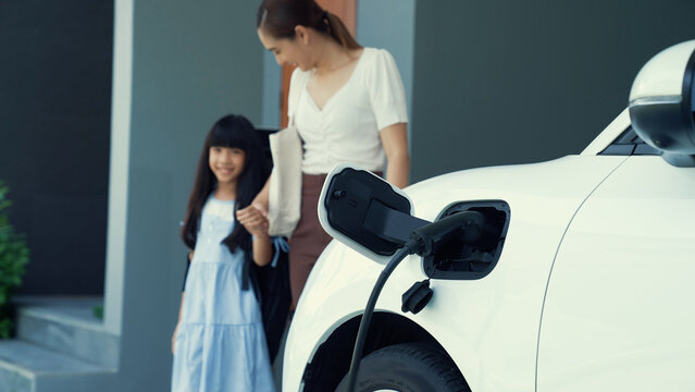 Progressive lifestyle of mother and daughter who have just returned from school in an electric vehicle that is being charged at home. Electric vehicle powered by sustainable clean energy.