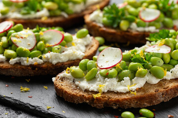 Soya bean and goats cheese sourdough bruschetta served with lemon zest and reddish on black slate board