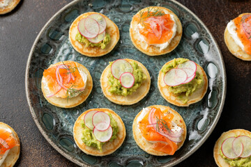 Mini blini pancakes with soft cheese, cold smoked salmon and guacamole