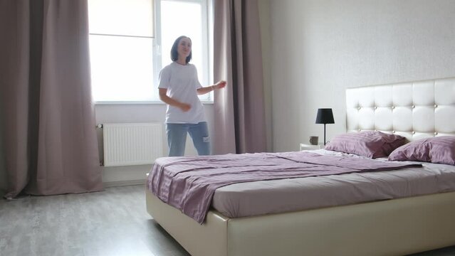 A cute woman is dancing and relaxing in her bedroom.