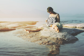 surreal woman moves the hands of a gear clock,.sitting on a rock in the middle of a lake