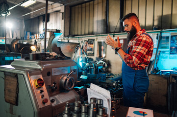 A young worker examining an object in his hands, next to a lathe machine.