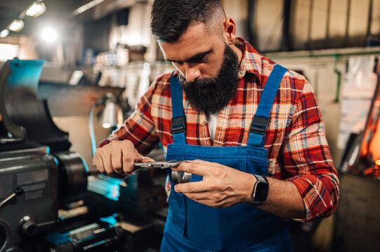 A metal turner using calipers to measure width of a cylinder in a factory. - Powered by Adobe