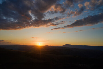 A beautiful golden sunset in the mountains. The sun is sinking behind the mountains, coloring the horizon with rays. Shooting from a drone.