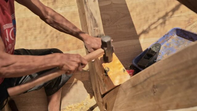 A shipbuilder hammering the frame of a traditional wooden fishing boat on the coast of Indonesia. Close up shot without showing the face. 