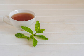 Fresh mint and cup of tea on white wooden background with copy space.