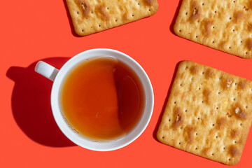 Cup of tea, crackers on red background with copy space. Food for breakfast.