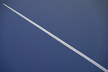 Flugzeug fligt diagonal und zieht Kondensstreifen hinter sich her.