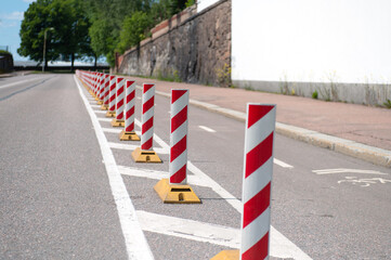 a row of light reflective red-white posts on the road, duplicating the markings separating the roadway from the bike path. Sunny summer day