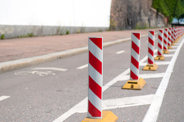 a row of light reflective red-white posts on the road, duplicating the markings separating the roadway from the bike path. Sunny summer day