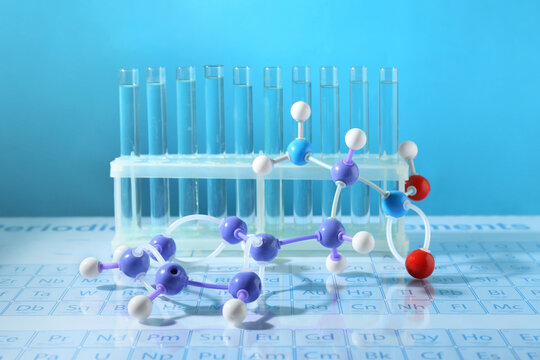 Molecular model and test tubes on periodic table against light blue background