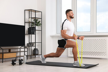 Athletic man doing exercise with elastic resistance band on mat at home