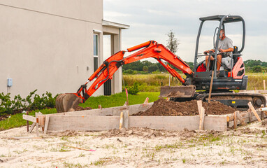  Front view of, an adult, male, digging with a tow able backhoe, moving dirt into a slab, wood form