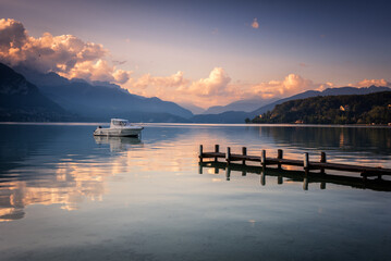 Boat next to a dock in the calm waters of Lake Annecy and the Alps mountain range in the background at sunset, Lake Annecy, Auvergne - Rhône - Alps, France, Europe