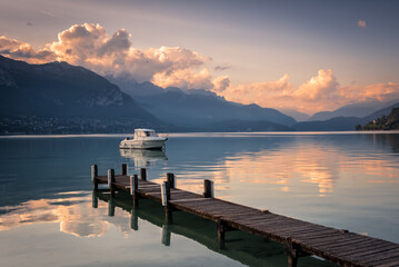 Boat beside a pier in the quiet waters of Lake Annecy and the Alps mountain range in the background at sunrise, Lake Annecy, Auvergne - Rhône - Alps, France