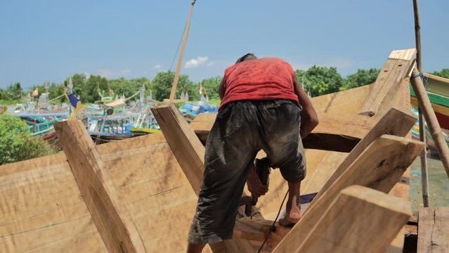 A shipbuilder is drilling the triangular section of a traditional wooden fishing boat frame on the coast of Indonesia. Close up shot without showing the face.