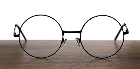 Round glasses with metal frame on wooden table against white background