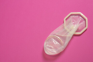 Unrolled female condom on pink background, top view and space for text. Safe sex