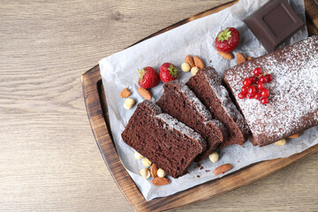 Tasty chocolate sponge cake with berries and nuts on wooden table, top view. Space for text