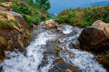 Raging water of a fast mountain river in a picturesque beautiful mountainous area, flowing water with splashes, selective focus