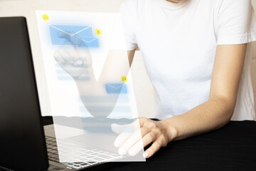 A girl touches a virtual window with an envelope with her hand while working at a laptop on a work...
