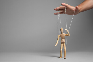 Man pulling strings of puppet on gray background, closeup. Space for text - obrazy, fototapety, plakaty