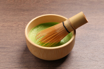 Cup of matcha tea and bamboo whisk on wooden table