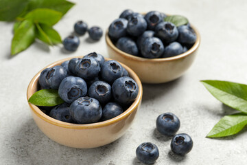 Tasty fresh blueberries in bowls on light grey table, closeup