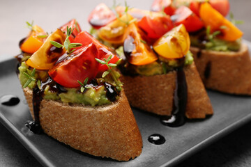 Delicious bruschettas with avocado, tomatoes and balsamic vinegar on gray plate, closeup