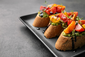 Delicious bruschettas with avocado, tomatoes and balsamic vinegar on gray table, closeup. Space for text