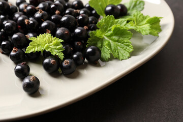 Plate with ripe blackcurrants and leaves on dark background, closeup