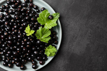 Plate with ripe blackcurrants and leaves on grey background, top view. Space for text