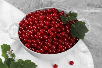 Ripe red currants and leaves in colander on grey textured table, closeup