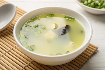 Bowl of delicious miso soup with tofu served on white wooden table, closeup