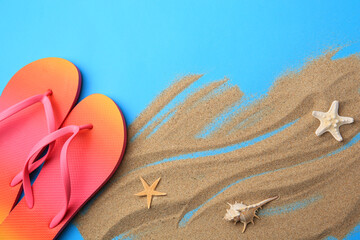 Fototapeta na wymiar Flip flops and sand on light blue background, flat lay. Beach accessories